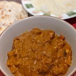 butter chicken in a porcelain bowl, red serving mat and naan bread