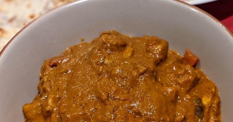 butter chicken in a porcelain bowl, red serving mat and naan bread